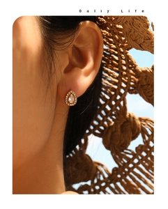 Detail of pear-shaped gold stud earring with pave stones shown on model