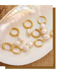 Détail de boucles d'oreilles torsadées dorées et perles d'eau douce dans un coquillage