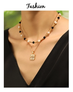 Detail of layered gold necklace featuring a pearl bead chain and square evil eye pendant