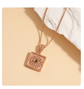 Detail of a gold square evil eye pendant necklace with a green gem on a stone backdrop