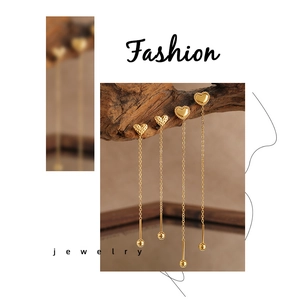 Detail showing golden heart-shaped tassel earrings with textured finish on wood