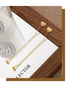 Detail of gold heart stud earrings with elegant long tassel chains and polished beads