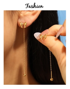 Close-up of gold bow tassel earrings with fine metal chains and polished beads