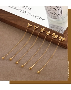 Detailed view of long gold tassel earrings with bow, leaf, and antler charms on wood