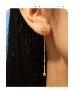 Detail of heart stud long chain earrings with gold ball pendant on female model ear
