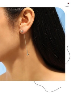 Detail of silver heart tassel earrings worn by a model against a light blue background