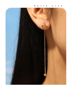 Macro shot of gold-plated maple leaf stud earrings with long chain tassel and small ball