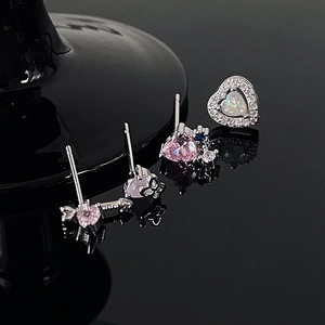 Sparkly heart and arrow earring set with pink and opal stones on a black reflective surface