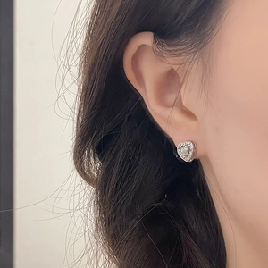 Macro view of heart-shaped earring with silver metal, sparkling zircons and mother of pearl