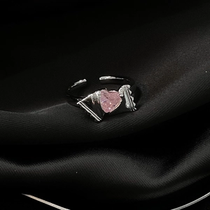 Makroaufnahme eines Rings mit rosa Herz-Edelstein und schwarzem Metall auf dunkler Seide
