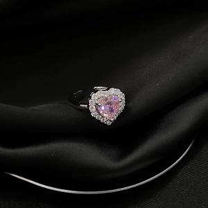 Makroaufnahme eines rosa herzförmigen Edelsteinrings mit Kristallhalo auf schwarzer Seide
