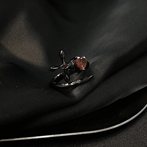 Détail de bague gothique avec croix et zircon rouge en cœur sur métal noir poli