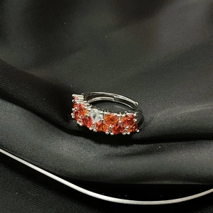 Detalle de anillo plateado con piedras naranjas sobre tela de seda negra mate