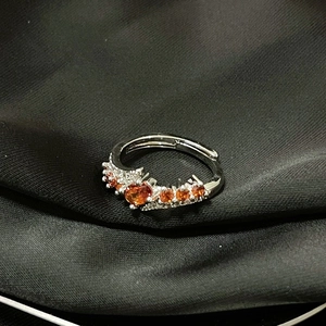Primer plano del anillo ajustable de plata con piedra naranja sobre seda negra