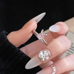 Nahaufnahme eines Rings mit rosa Zirkon und Hasenohren an Hand mit Paillettennägeln