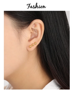 Gros plan de boucles d'oreilles boules dorées minimalistes portées en ensemble tendance