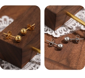 Vue détaillée de boucles d'oreilles boules dorées et argentées sur bois et dentelle