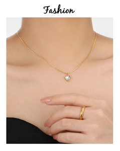 Gros plan du collier coeur en pierre de lune dorée et de la bague en spirale portée
