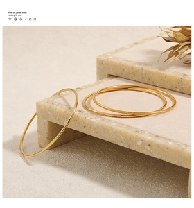 Macro detail of three minimalist gold stackable bracelets with polished and frosted finishes