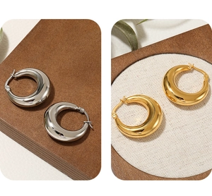Detailed comparison of wide gold and silver crescent hoop earrings on wooden tray