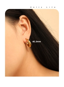 Detail of 2.3mm thick gold-tone minimalist hoop earrings shown on a female model