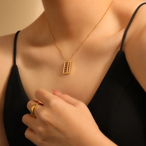 Golden abacus pendant necklace and minimalist ring set shown on model in warm lighting