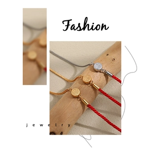 Detail of red braided cord bracelet with gold Fu character charm and snake bone chain