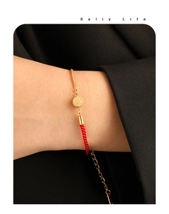 Detailed macro of a braided red rope and gold chain bracelet with a Fu character charm