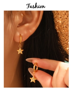 Close-up of gold star earrings with sparkling zircon crystals on a model wearing a straw hat