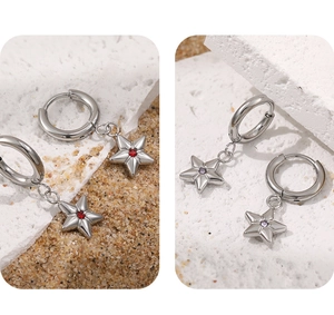 Detail of silver star hoop earrings with red and purple zircon stones on a sandy background