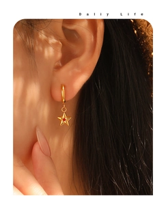 Close-up of star-shaped gold-plated earring with red zircon on model's ear