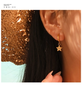 Close-up of golden star drop earrings with purple zircon on a model in sunny summer setting