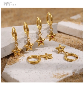 Detail view of 24K gold plated star earrings with colored zircon on a textured stone