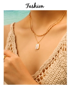 Close-up of double layered gold necklace with shell pendant on a model in beach setting