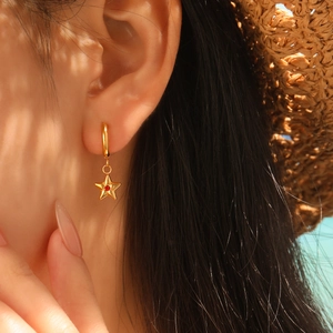 Elegant 24K gold-plated star earrings with red zircon worn by a model in soft sunlight