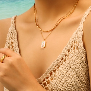 Layered gold bead necklace with rectangular shell pendant worn on a summer beach resort