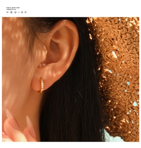Gros plan de boucles d'oreilles créoles en acier titane doré avec zircons sur un mannequin
