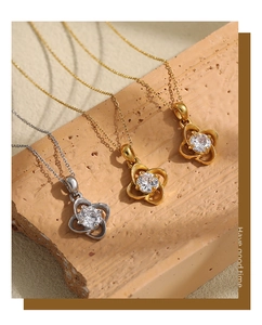Detail view of gold clover necklace with zircon center on a textured stone surface