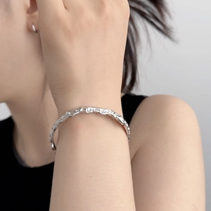 Dettaglio del bracciale aperto in argento con texture lava e orecchino in metallo minimal