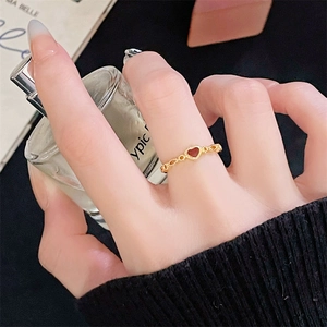 Close-up of a vintage hollow gold ring with a red heart on a model holding perfume