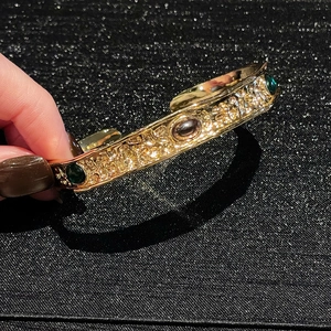 Detailed close-up of vintage hammered gold cuff bracelet with green and brown gemstones