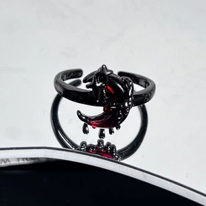 Detail of gothic moon ring with red stone and black alloy finish on reflective surface