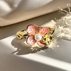 Detalle de anillo de flor dorada con esmalte rosa y perlas sobre seda suave