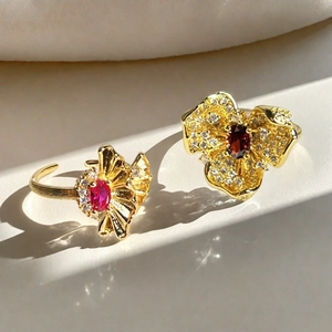 Detalle de anillos de flores vintage con gemas rojas y textura de oro cepillado fino