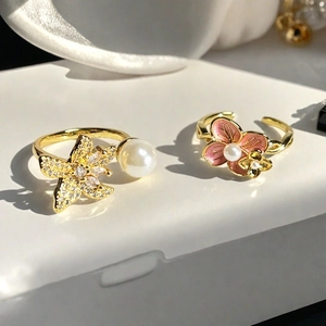 Detalle de anillos de flores doradas con perlas y esmalte rosa en soporte blanco