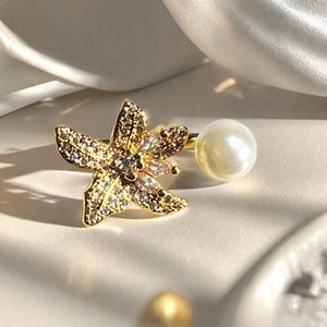 Detalle macro de anillo de estrella de mar dorada con pavé de cristales y perla en seda