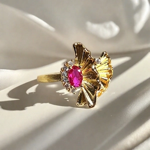 Detalle de anillo dorado vintage con piedra magenta y detalles texturizados de hojas de ginkgo