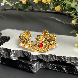 Detailansicht eines Goldkronenrings mit rotem Zirkonia und Perlen auf dunklem Stein