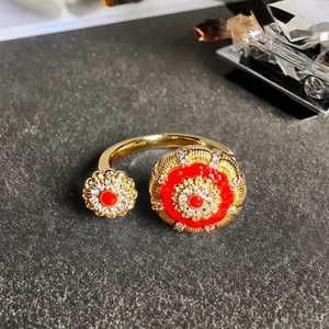 Makro-Detailansicht des goldenen Blumenrings mit rotem Emaille und weißen Zirkonias