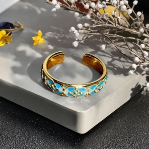 Nahaufnahme eines goldenen Rings mit blauem Emaille-Blumenmuster auf einer Steinfläche